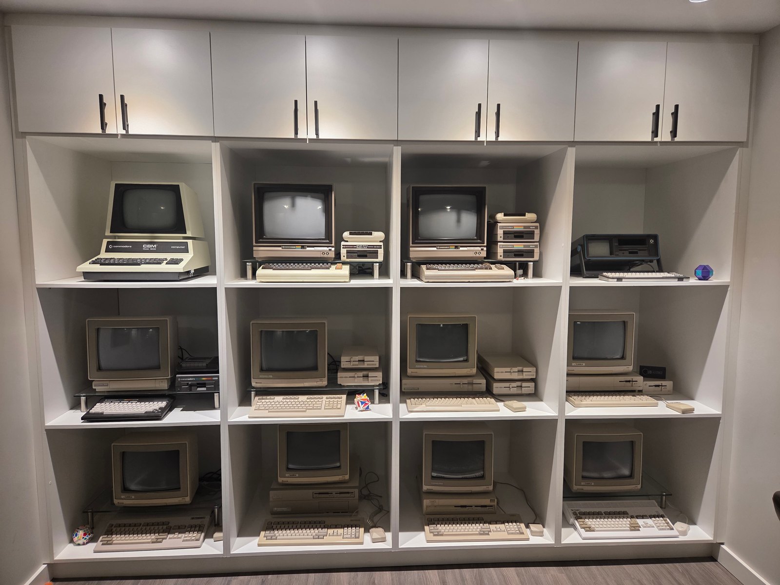 A large wall of white shelving filled with vintage computers — a Commodore PET, monochrome-monitor systems and compact Macs arranged in a grid
